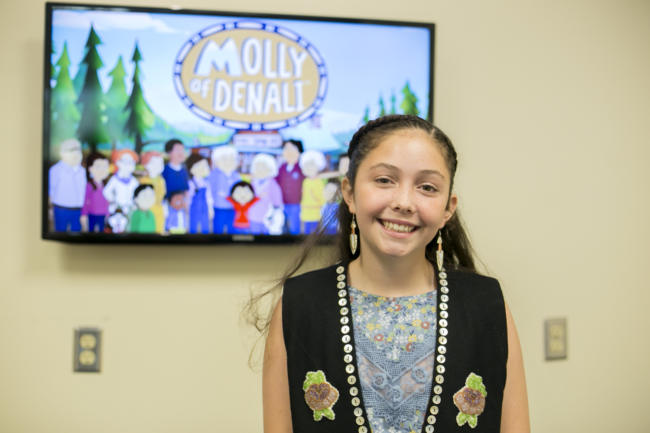 A girl in a black vest stands in front of a tv screen. Tlingit and Muckleshoot actress Sovereign Bill poses at a voice-over workshop at KTOO Public Media before the Juneau premiere of the PBS KIDS show "Molly of Denali" Saturday, August 10 at 9:30 a.m. at Elizabeth Peratrovich Hall.