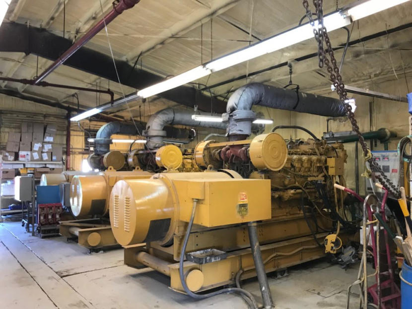 Two large diesel generators, painted yellow and sitting in a warehouse-style facility.