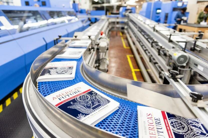 Copies of the president's fiscal year 2021 budget move down a conveyor belt.
