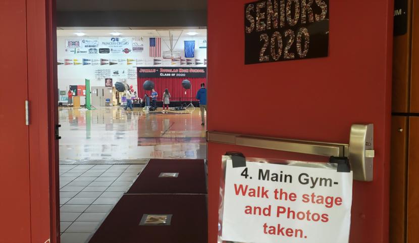 Photographers, school staff and the graduation stage stand by in the gym of Juneau-Douglas High School: Yadaa.at Kale between graduates on May 18, 2020.