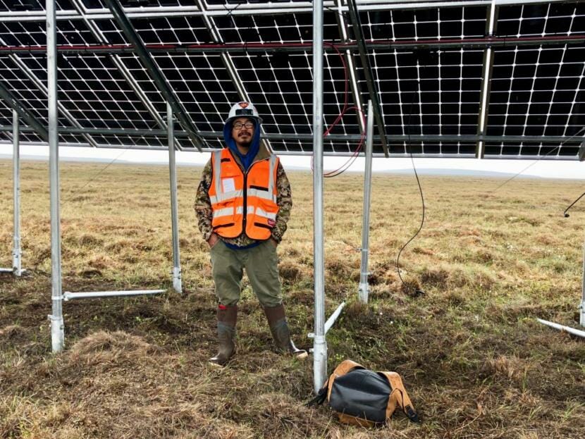 A man in an orange vest stands in front of a solar panel array