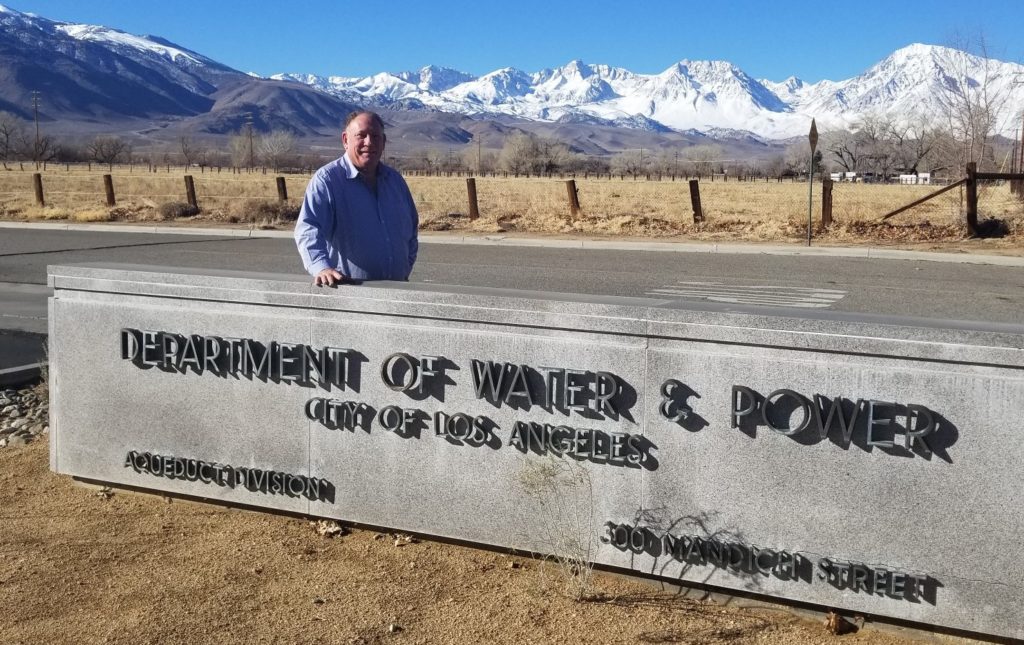 LA Aqueduct Manager stands behind LADWP Bishop office sign outside.