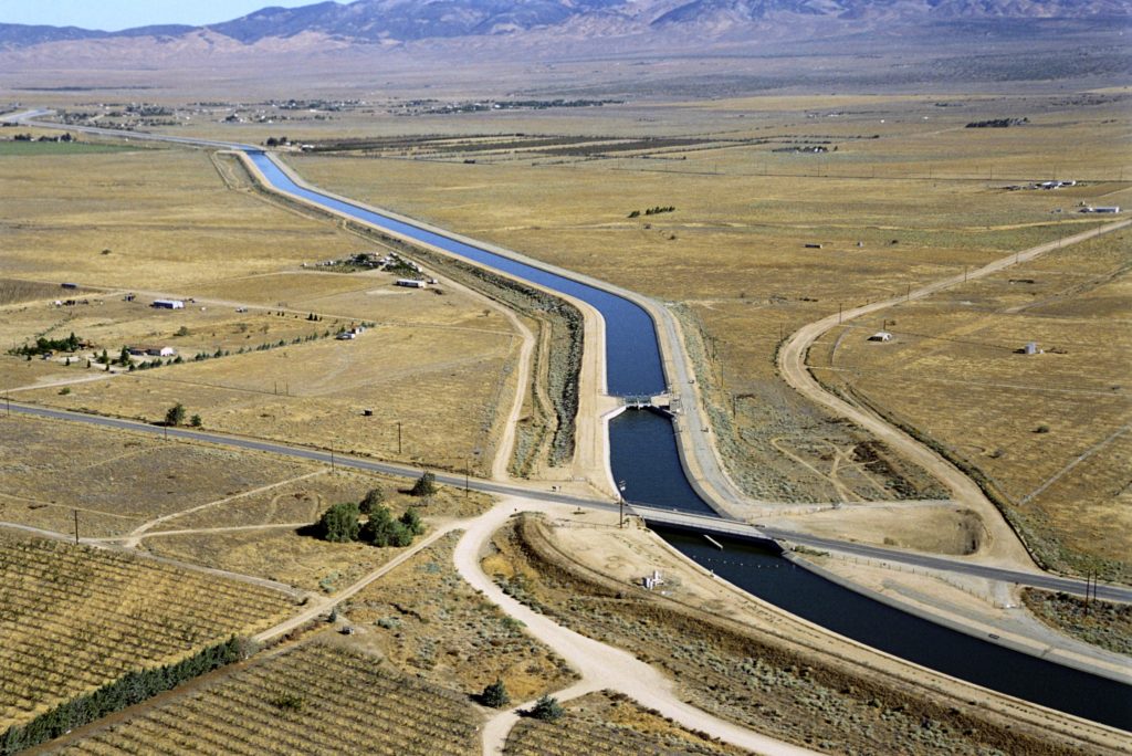 Water in aqueduct making its way across desert with mountains in the background