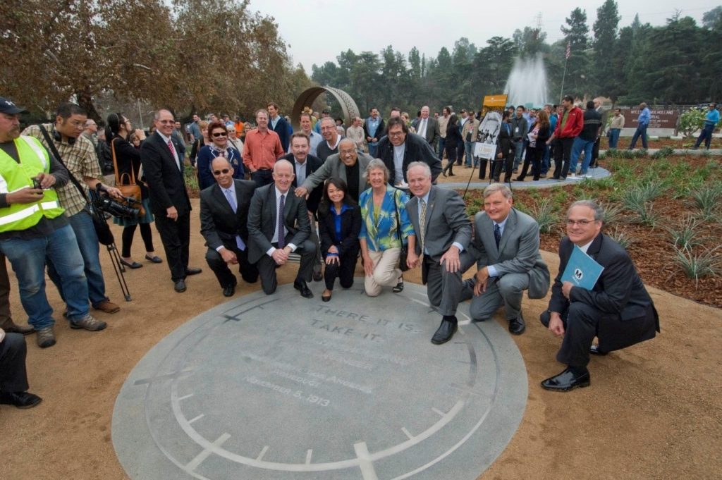 A group of people kneeling around a large circular commemorative plate with more groups of people in the background
