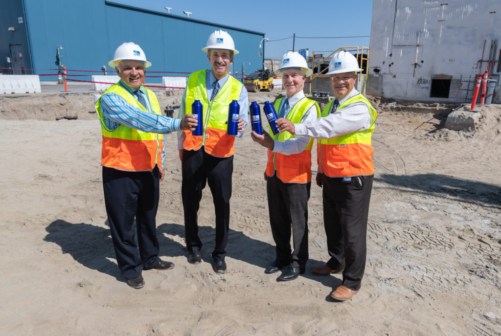 Image of four men in hard hats and construction vests holding blue water bottles