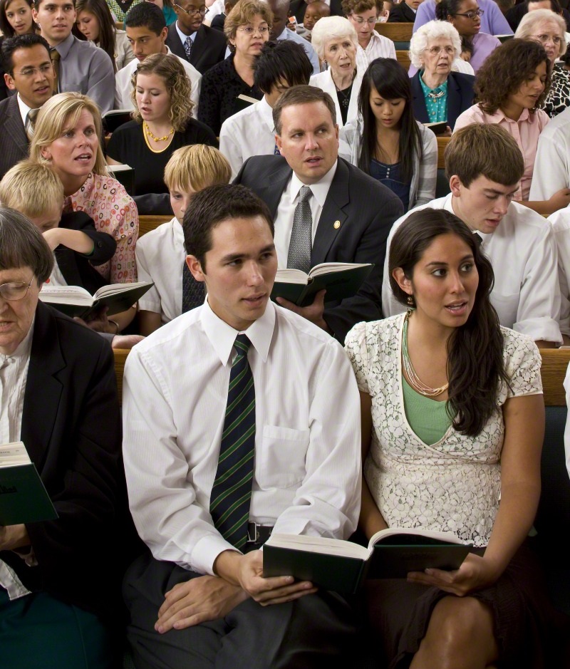 Two LDS singles sit anxiously on the front row in a family ward meeting. 