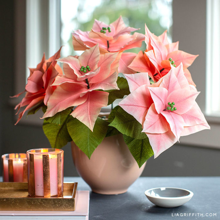 pink crepe paper poinsettia plants in vase next to candles on table