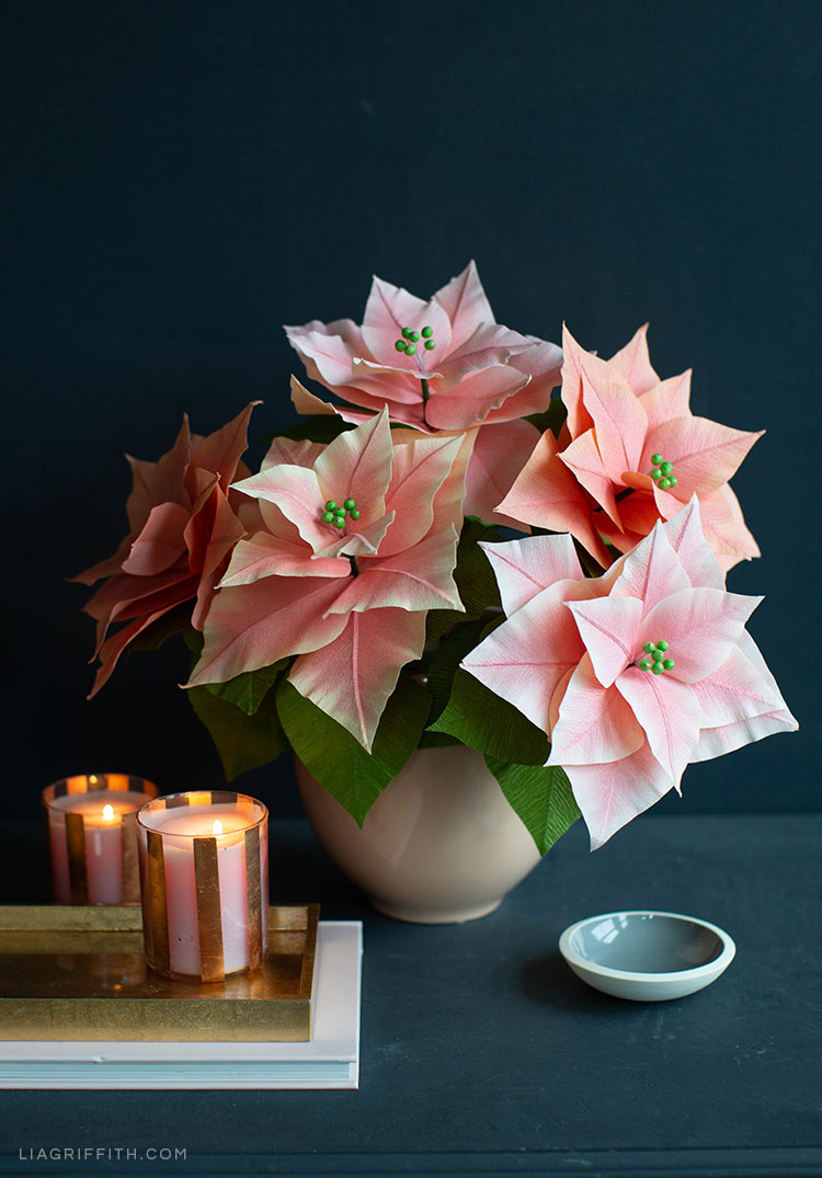 pink crepe paper poinsettia plants in vase next to candles and small dish