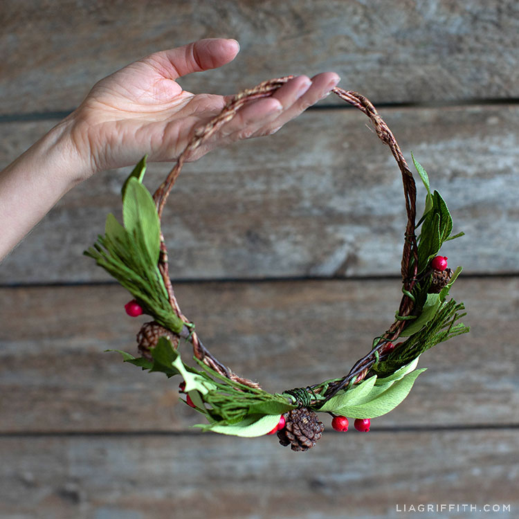Hand holding crepe paper evergreen head wreath with holly berries and pine cones