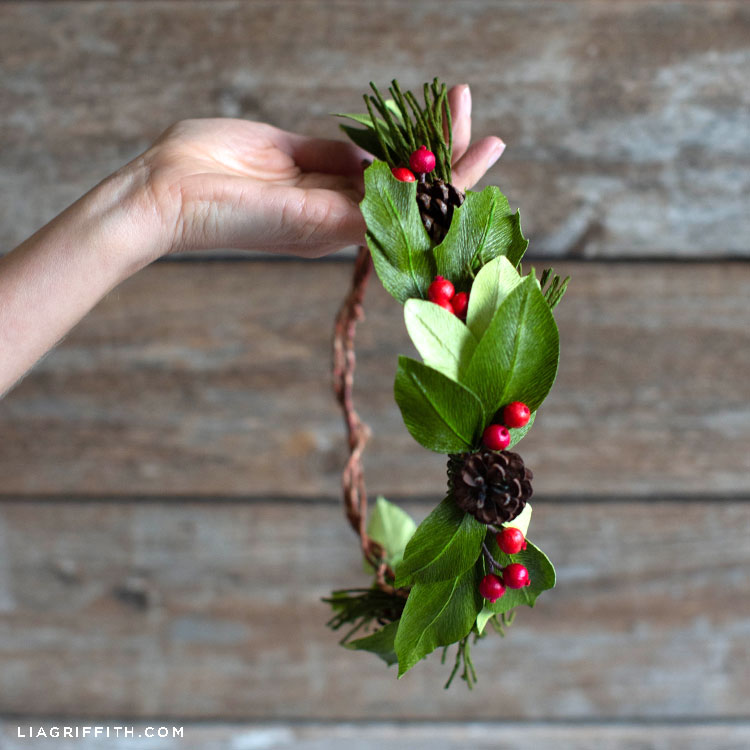 Hand holding crepe paper evergreen head wreath with holly berries and pine cones