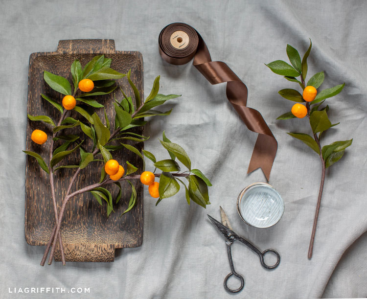 crepe paper kumquat branches on wood tray next to scissors and brown ribbon