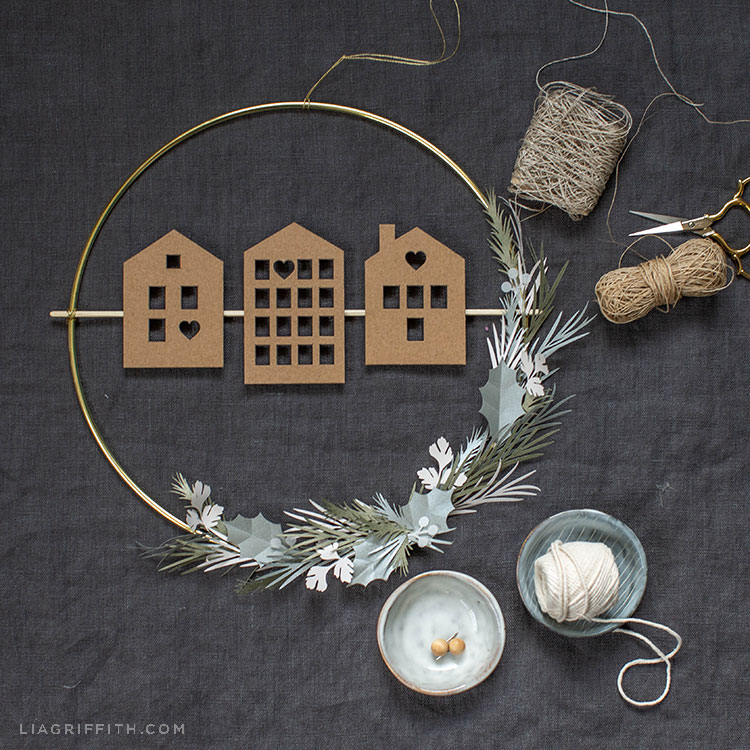 Scandi house and greenery wreath on grey sheet next to twine and scissors