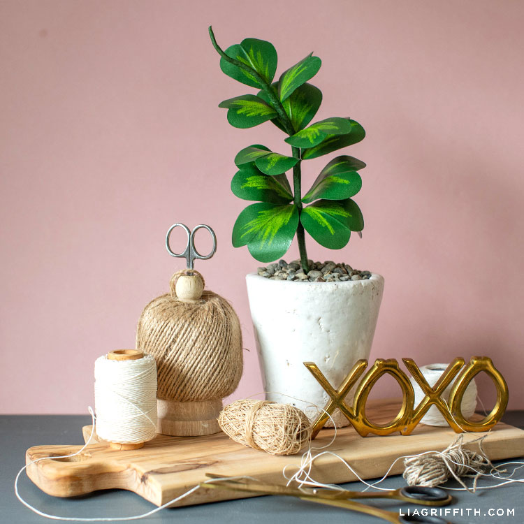paper Hoya Kerrii plant in white pot on wooden board next to XOXO sign, twine, and scissors