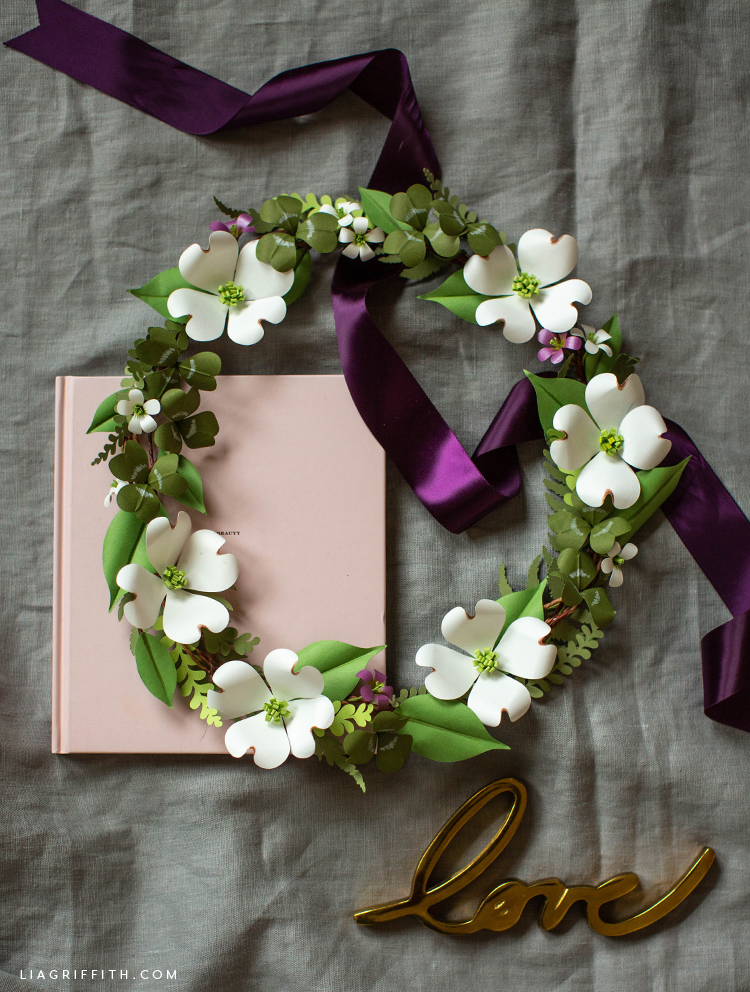paper shamrock and dogwood wreath with purple ribbon and pink book on grey sheet