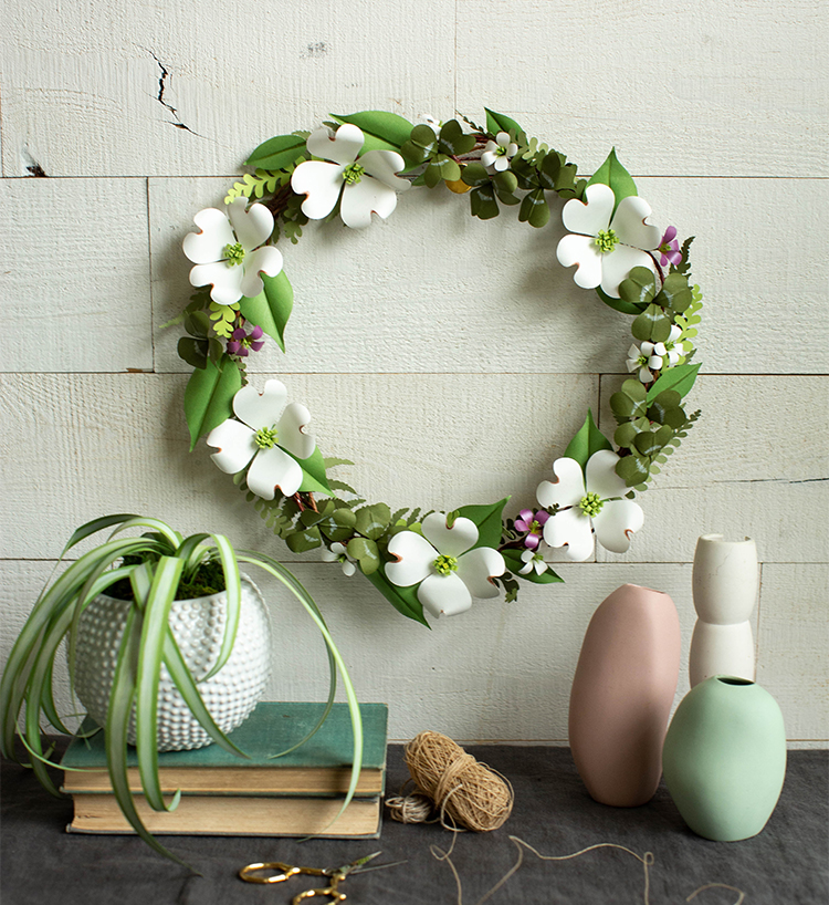 paper shamrock and dogwood wreath on white wall above paper plant, vases, and books