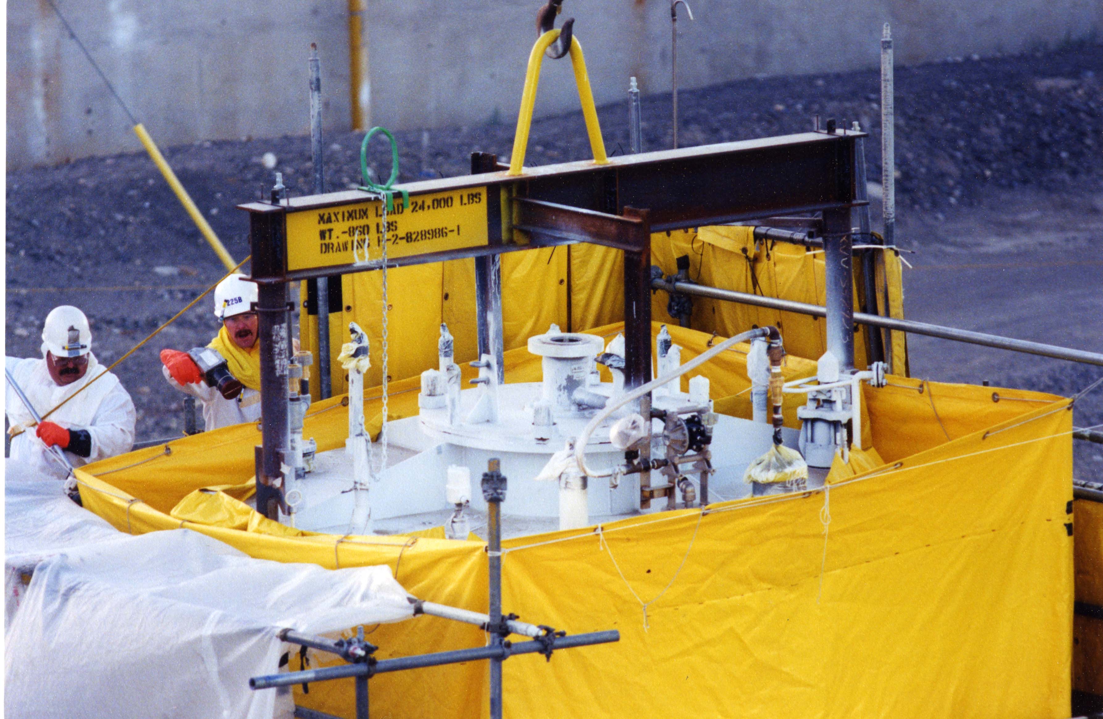 Device with Tarp Around it and Men Working on it with Sign · Hanford