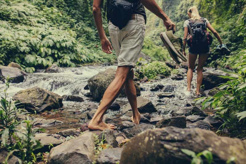 Couple-walking-by-the-creek-in-forest-with-their-shoes-in-hand.jpg