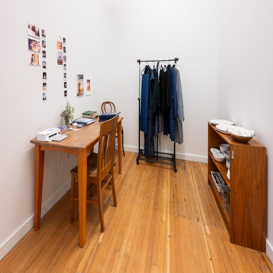 A minimalist room with a wooden desk, chair, and clothing rack, alongside a shelving unit with dishes.