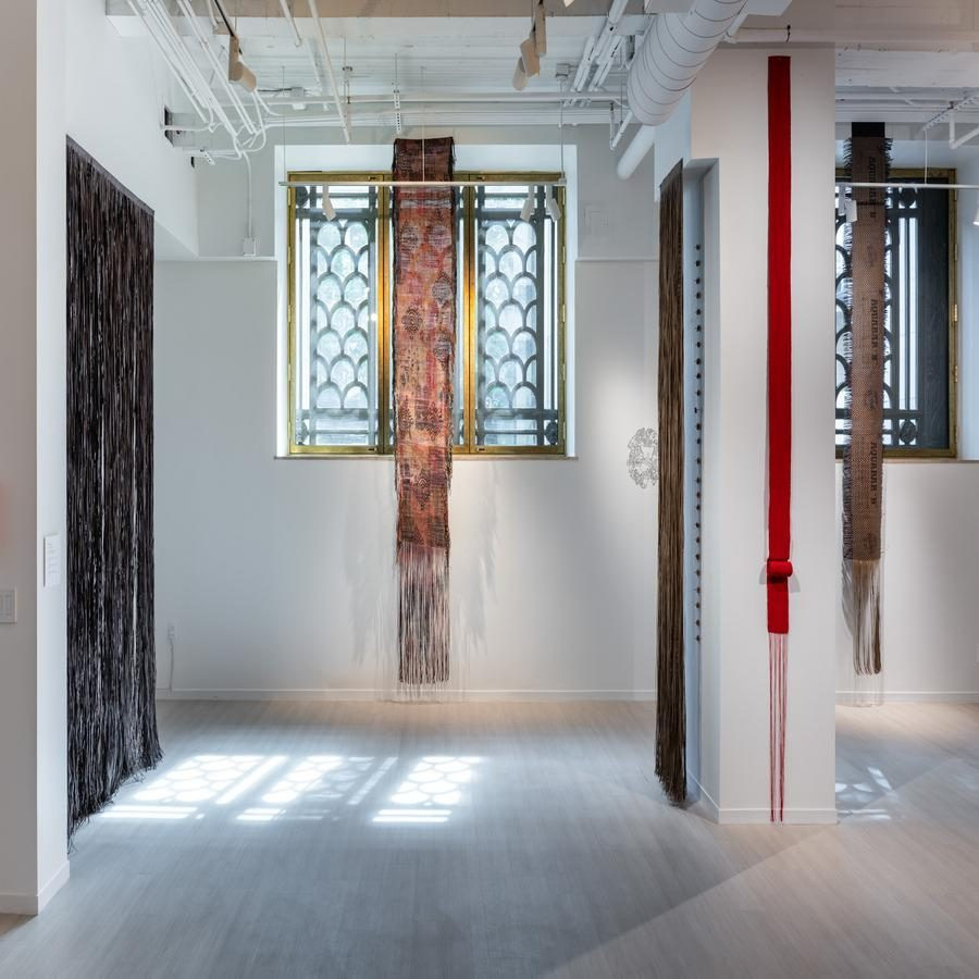 Textiles hanging in front of patterned windows, featuring earthy and red tones.