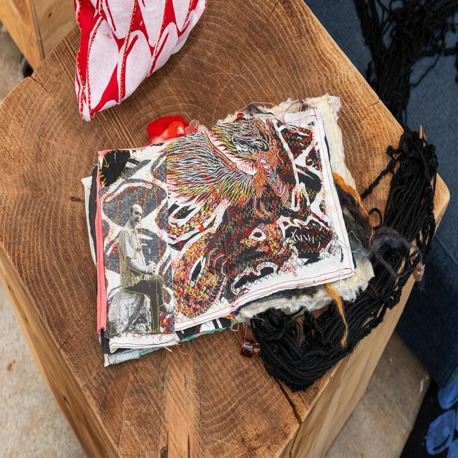 Open embroidered textile book with a black and white photo on a wooden surface, surrounded by yarn.