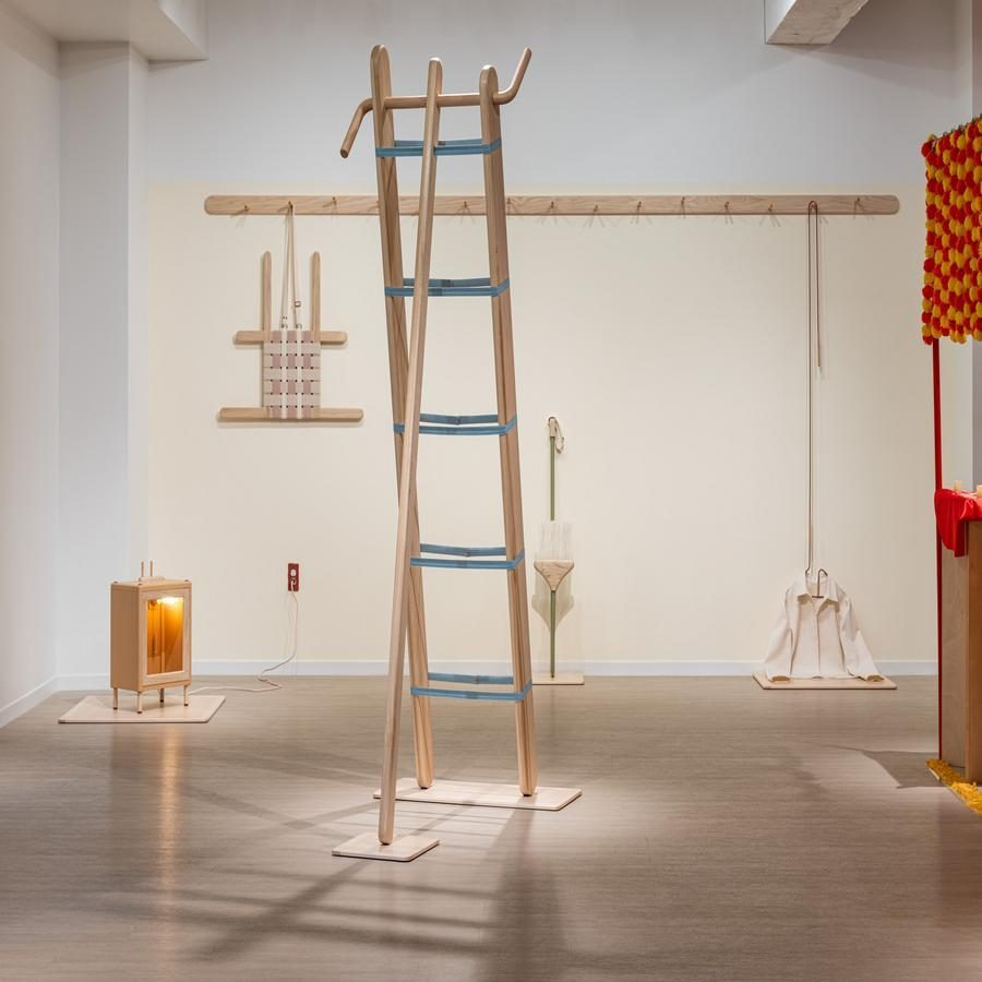 Art exhibition featuring a wooden ladder-like sculpture with blue bands, a lit wooden box, and other minimalist pieces.