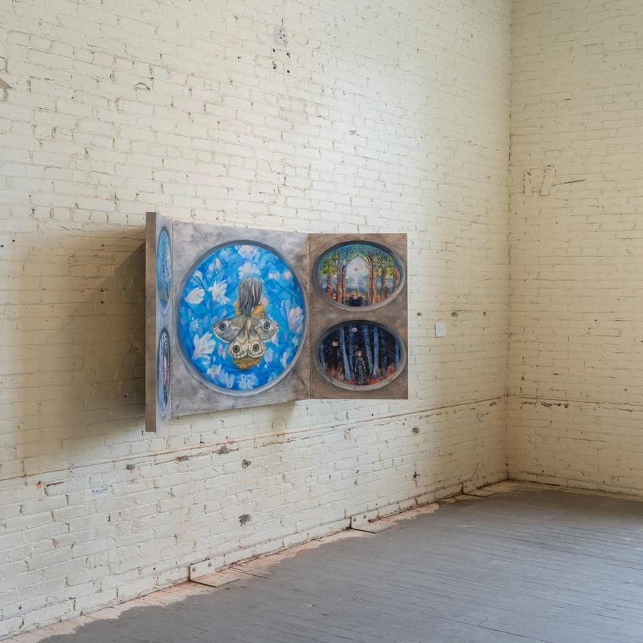An artwork with three circular panels mounted on a cream brick wall in a gallery space.