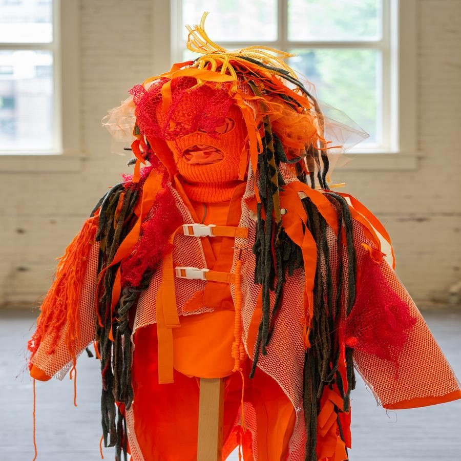Orange and red abstract costume with various textured fabrics in a gallery space.
