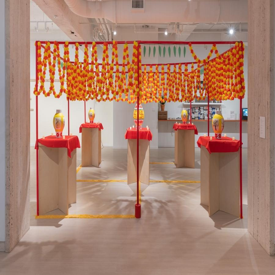 Art installation featuring marigold garlands and painted vases on pedestals.