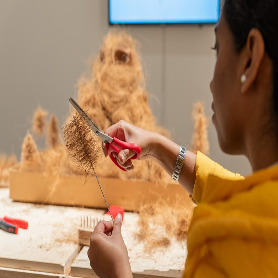 Person using red-handled scissors to cut fibrous material in an art installation.