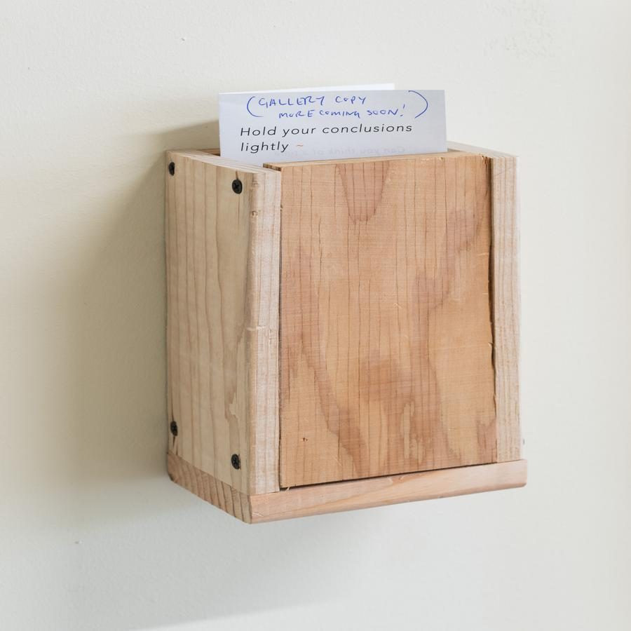 A small wooden box on a wall with a paper protruding from the top.