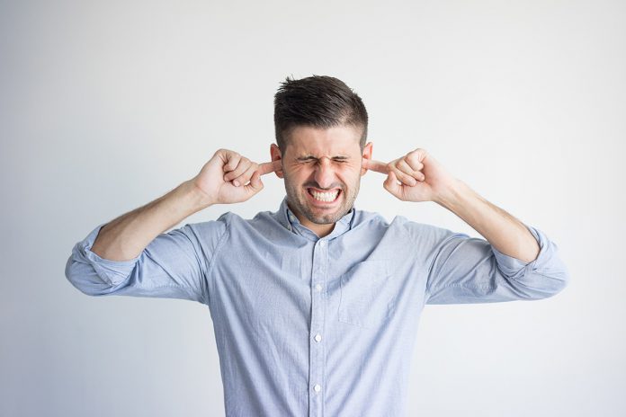 Portrait of irritated young man plugging ears with fingers