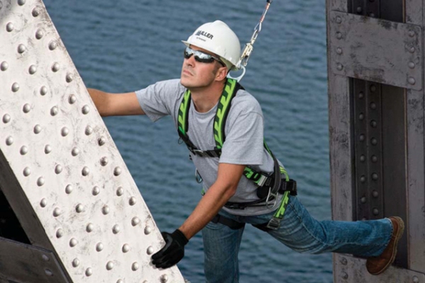 A man wearing a safety harness for fall protection working on a bridge while suspended in the air.