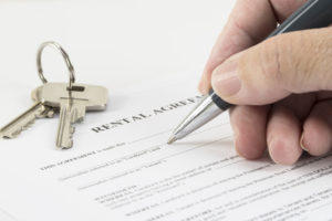 hand is writing with a pen on a rental agreement document, house keys in the background