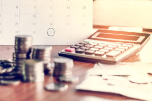 calendar with date circled when bills are due with calculator and cash on table