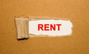 The text Rent appearing behind torn brown paper
