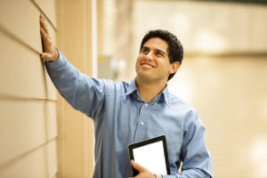 man inspects outside of building holding digital tablet