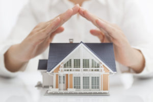 model of house with person standing behind protecting it with their hands