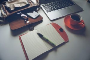 Laptop next to a cup of coffee and a blank notepad