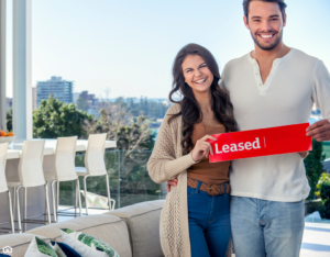 Young couple holding a leased rental sign in a luxury home