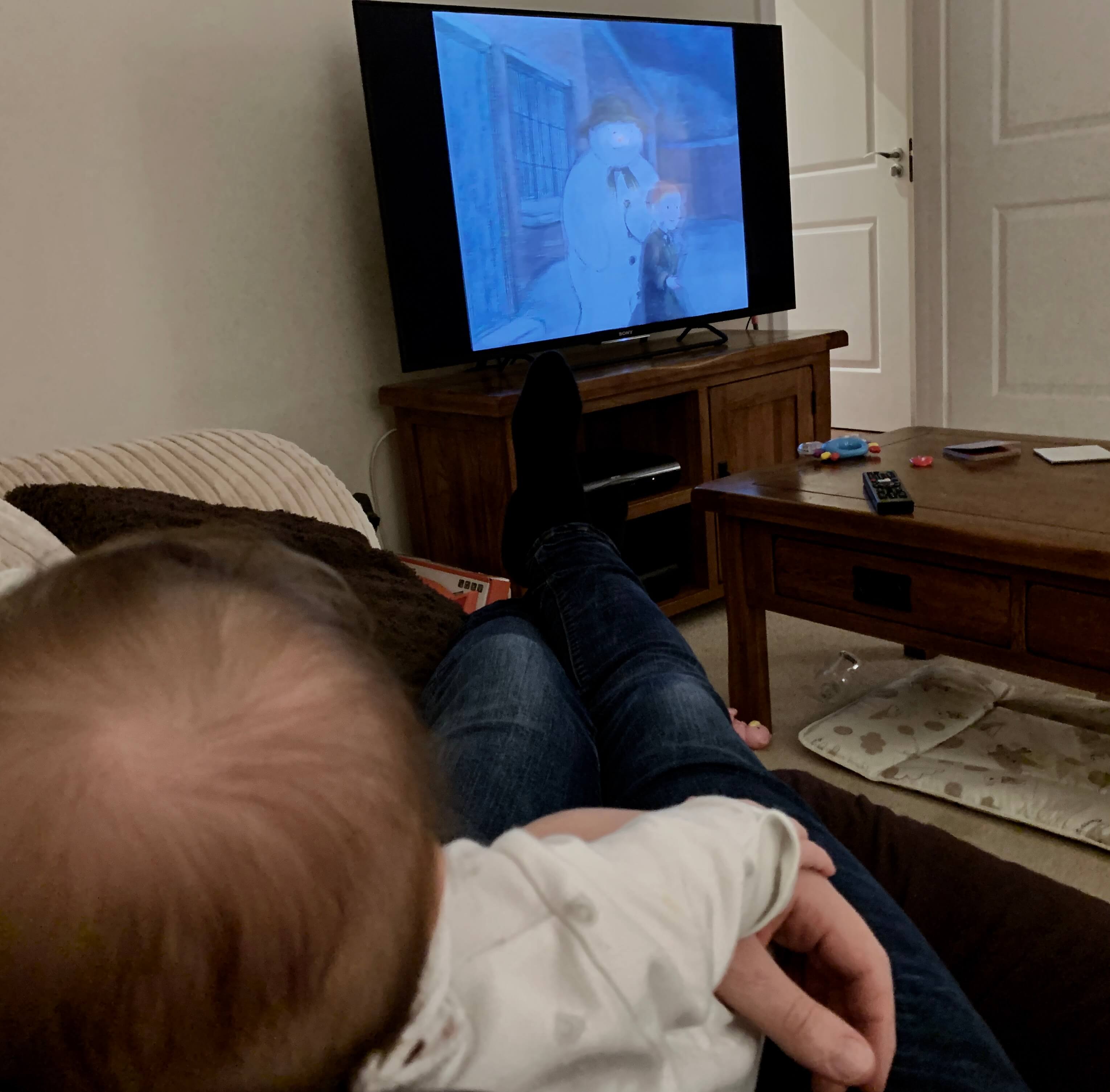 A baby in the foreground watches The Snowman in the background