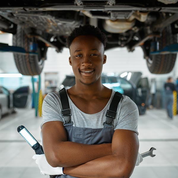autotech student with wrench and light standing beneath car