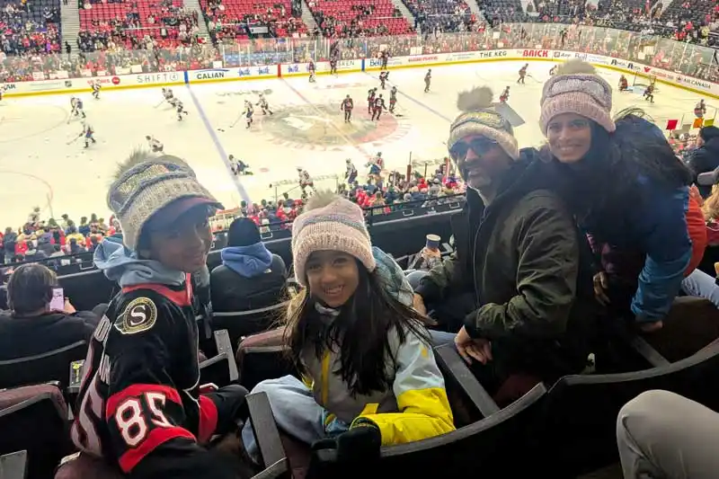 a family of four in the stands with a ice hockey game in the background
