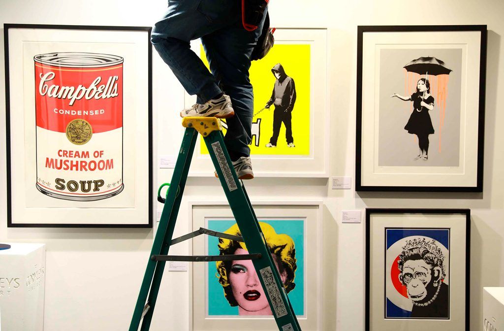 Un trabajador ajusta la iluminación de varias piezas de Andy Warhol y Bansky expuestas en al feria que conmemora su 30 aniversario. LAPRENSA/EFE/ Neil Hall