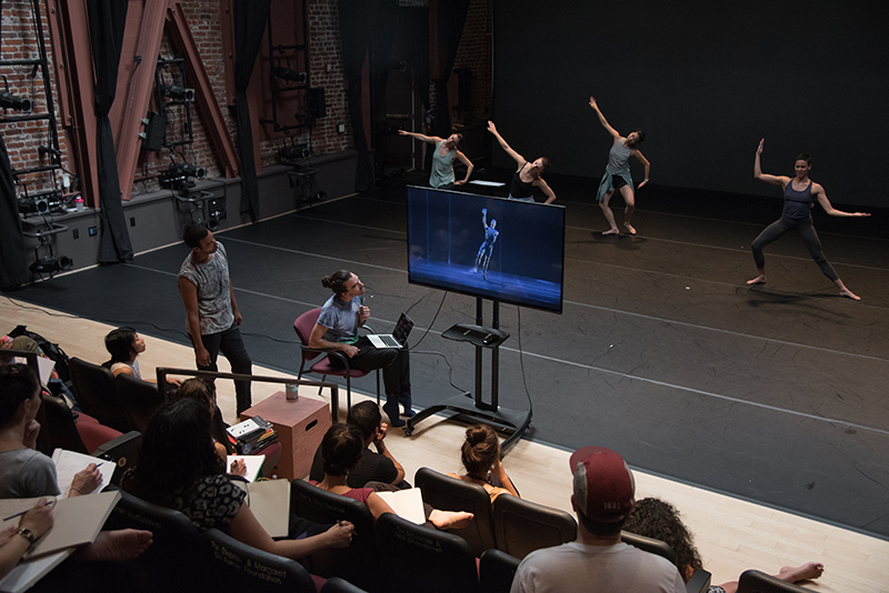 The commissioned artists watch footage from the Cunningham archives while the dancers rehearse on stage.