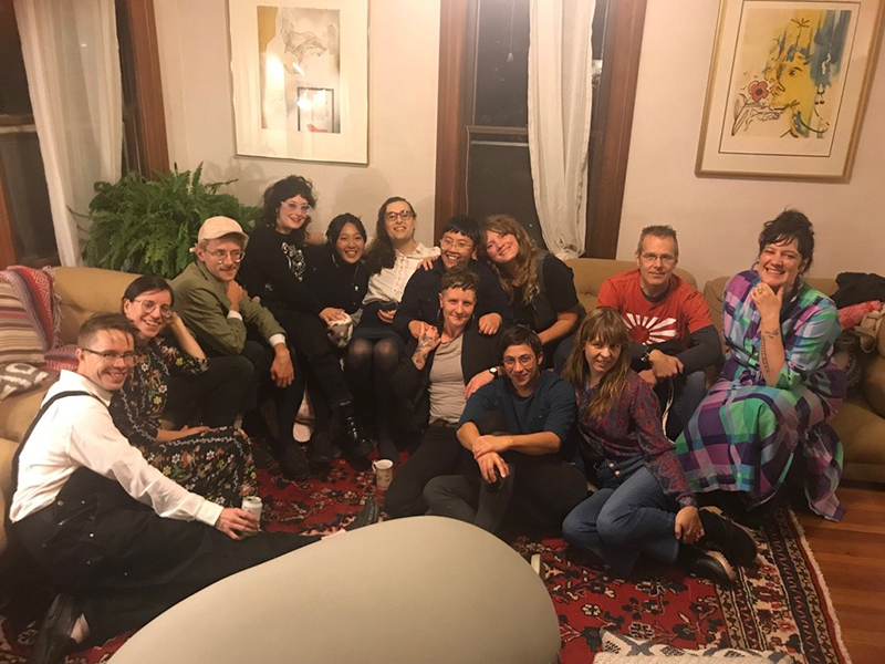From left to right: Ted Rees, Olive Blackburn, JJ Mull, Sara Wintz, Trisha Low, Zoe Tuck, Cheena Marie Lo, Tessa Micaela, Rebecca Maillet, Syd Staiti, Stephanie Young, Clay Banes, and Brittany Billmeyer-Finn. Pictured in Zoe and Brittany's living room in Northampton, MA on Friday, October 25, 2019, when Ted, Trisha, Syd, and Stephanie visited from the Bay Area to read from their books. Ted, Olive, JJ, Sara, Cheena, Tessa, Rebecca, Clay, Brittany, and Zoe met in the Bay Area and live constellated across MA, VT, RI, and PA now. Photo by Jay Weingarten.