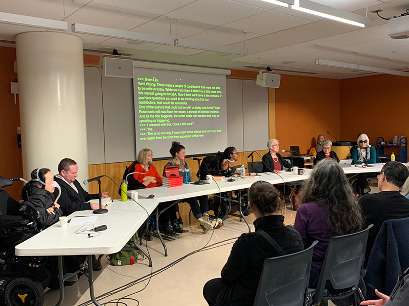 Book event at the San Francisco Public Library. In the foreground is a row of people sitting in chairs. In the background is a row of panelists sitting at tables with microphones with a screen showing the transcription of the event in real-time.