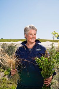 A woman standing outside holding different native plants.