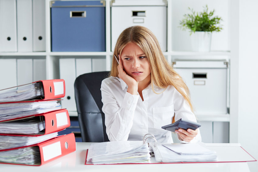 Pensive business woman calculates taxes at desk in office