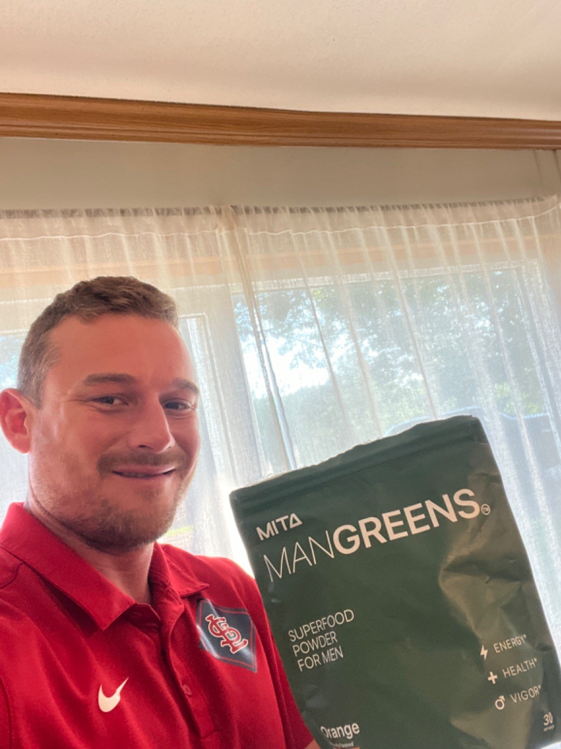 Man in red shirt holding a bag of Mita ManGreens superfood powder for men.