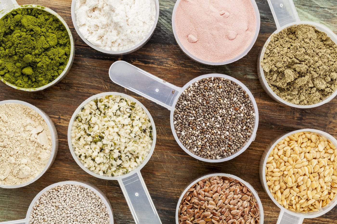 scoops of superfood - healthy seeds and powders (white and brown chia, brown and golden flax, hemp, pomegranate fruit powder, wheatgrass, hemp and whey protein, maca root) - top view scoops of superfood